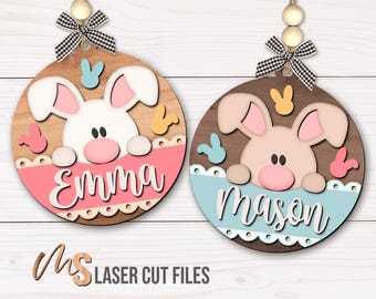 May include: Two round wooden Easter bunny ornaments with personalized names. The ornament on the left is pink with the name "Emma" and the ornament on the right is blue with the name "Mason".