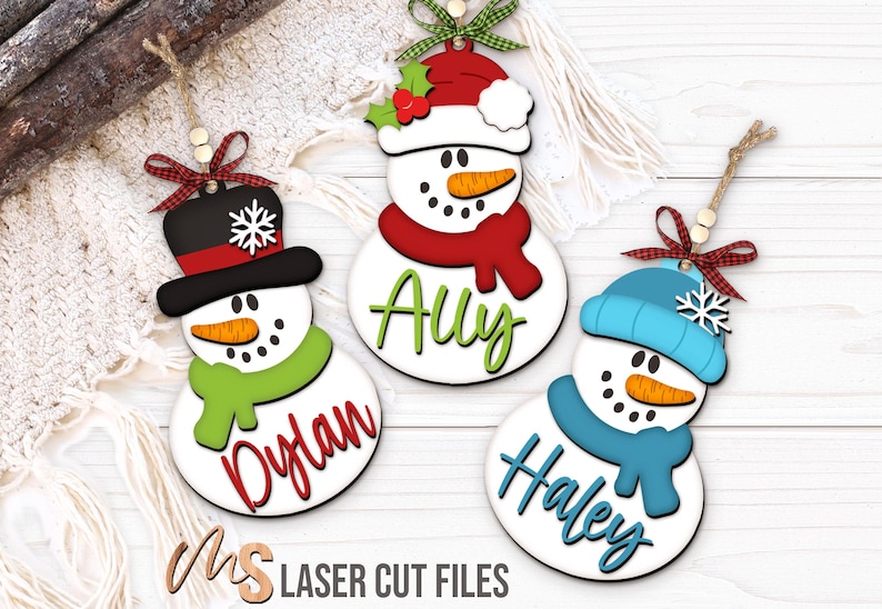 SVG Laser Cut Files for a bundle of three cute Snowman Ornaments wearing a santa hat, snowman hat, and winter beanie cap with scarfs, snowflakes, and an open space to add your own custom text and names. Perfect for making custom Christmas Ornaments, Christmas Gift Tags and Name Tags for the holidays!