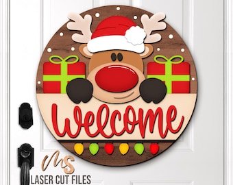May include: A round wooden Christmas door sign featuring a reindeer wearing a Santa hat and holding a "Welcome" sign. The sign includes two gift boxes and a string of lights. The sign is approximately 30 cm in diameter.