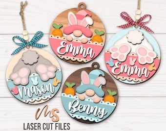 May include: Three wooden ornaments with bunny and gnome designs. Each ornament has a different name: Emma, Mason, and Benny. The ornaments are decorated with pastel colors and have a rustic woodgrain finish.
