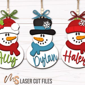 SVG Laser Cut Files for a bundle of three cute Snowman Ornaments wearing a santa hat, snowman hat, and winter beanie cap with scarfs, snowflakes, and an open space to add your own custom text and names. Perfect for making custom Christmas Ornaments, Christmas Gift Tags and Name Tags for the holidays!