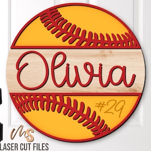 Puede incluir: Un letrero redondo de madera con un diseño de béisbol. El letrero es amarillo con costuras rojas y un borde rojo. El nombre "Olivia" está escrito en rojo en una tira de madera en el medio del letrero. El número "29" está escrito en amarillo en la parte inferior del letrero.