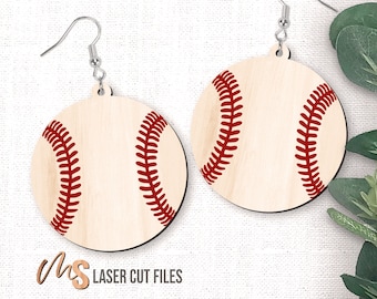 May include: A pair of wooden earrings shaped like baseballs with red stitching. The earrings are on a white fabric background.
