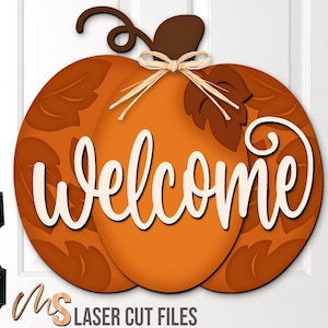 Op de afbeelding: Een houten deurhanger in de vorm van een pompoen met het woord "Welcome" in wit script. De pompoen is oranje met bruine accenten en blad details. Een bruine stengel en een raffia strik maken het ontwerp compleet. De tekst "MS LASER CUT FILES" staat onderaan.