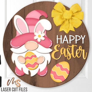 May include: A pink and white Easter gnome holding a yellow and pink Easter egg. The gnome is wearing a pink hat with bunny ears and a white flower. The background is a brown wooden circle with the text "Happy Easter" in yellow letters.