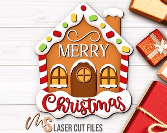 Könnte beinhalten: Ein Lebkuchenhaus-Weihnachtsdekoration mit den Worten "Merry Christmas". Das Haus ist braun mit weißem Zuckerguss und bunten Süßigkeiten-Akzenten. Mehrere verpackte Geschenke befinden sich im Hintergrund.