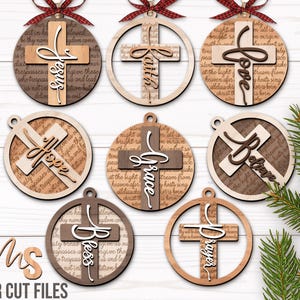 May include: A collection of laser-cut wooden Christmas ornaments. Each ornament features a cross design with words like "Jesus," "Faith," "Love," "Hope," "Grace," "Believe," "Bless," and "Prayer." The ornaments have a rustic, layered design with a red plaid ribbon.