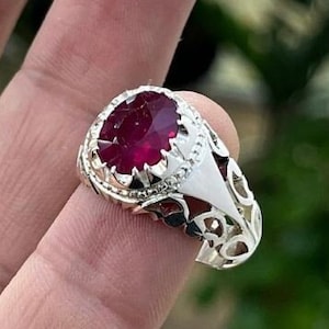 Puede incluir: Un anillo de plata con un diseño adornado y una gran piedra roja redonda.
