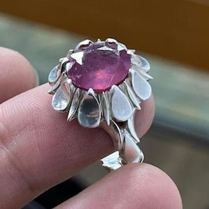 May include: A silver ring featuring a large, round, pink gemstone set in a flower-shaped design.
