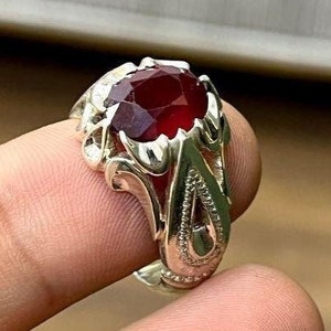Puede incluir: Un anillo de plata con un diseño adornado y una gran piedra roja.