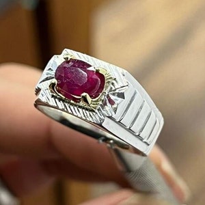 Op de afbeelding: Zilveren ring met een grote, ovaal geslepen robijn. De robijn heeft een dieprode kleur en is gezet in een gouden zetting. De ring heeft een getextureerd ontwerp op de band.