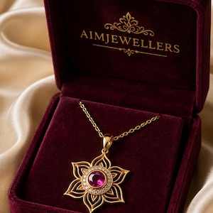 Peut inclure: Un collier en or avec un pendentif en forme de fleur, doté d'une pierre rose ronde centrale entourée de petites pierres blanches. Le pendentif repose dans un écrin en velours rouge foncé avec le texte doré AIMJEWELLERS sur le couvercle.