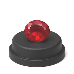 May include: A faceted, round, deep red gemstone sits atop a matte black pedestal. The gemstone's cut reflects light, showcasing its brilliance. The pedestal has a simple, tiered design, providing a contrasting backdrop for the jewel.