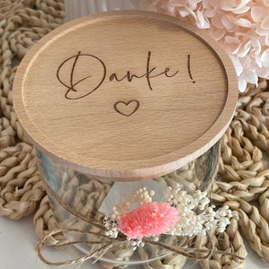 Può includere: Un coperchio di legno con la parola "Danke!" e un cuore inciso. Il coperchio è sopra un barattolo di vetro trasparente con fiori secchi all'interno.
