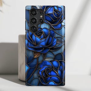 May include: A phone case with a stained glass design featuring blue roses. The case has a black border and a camera cutout.