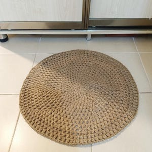 May include: A round, brown, woven rug made of natural fibers. The rug has a textured, crocheted design.