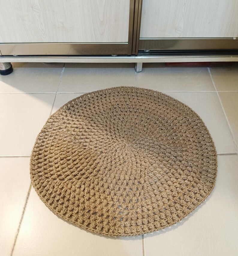 May include: A round, brown, woven rug made of natural fibers. The rug has a textured, crocheted design.