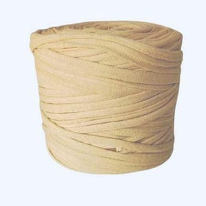 May include: A cylindrical spool of light beige fabric yarn wound in a continuous, flat, and flexible strip. The material has a smooth, matte texture and is coiled tightly to form a solid, uniform shape with visible horizontal layers throughout.