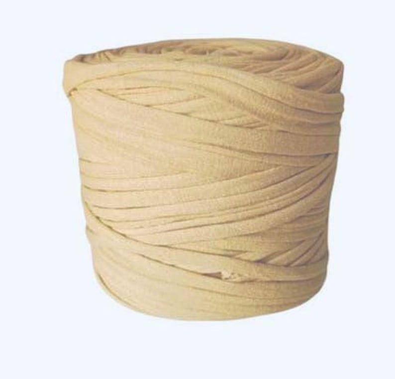 May include: A cylindrical spool of light beige fabric yarn wound in a continuous, flat, and flexible strip. The material has a smooth, matte texture and is coiled tightly to form a solid, uniform shape with visible horizontal layers throughout.