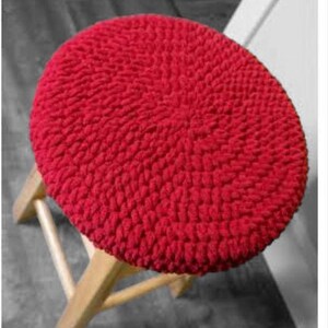Puede incluir: Coj&iacute;n de silla de crochet rojo. El coj&iacute;n es redondo y tiene una superficie texturizada.