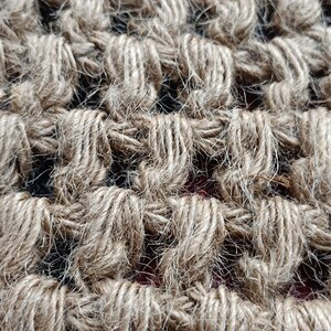 May include: Close-up of a woven jute rug with a natural brown color. The rug has a textured, rough surface and is made of tightly woven strands of jute.