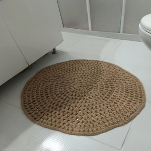 May include: A round, beige, crocheted rug with a textured pattern. The rug is made of natural fibers and has a rustic, handmade look.
