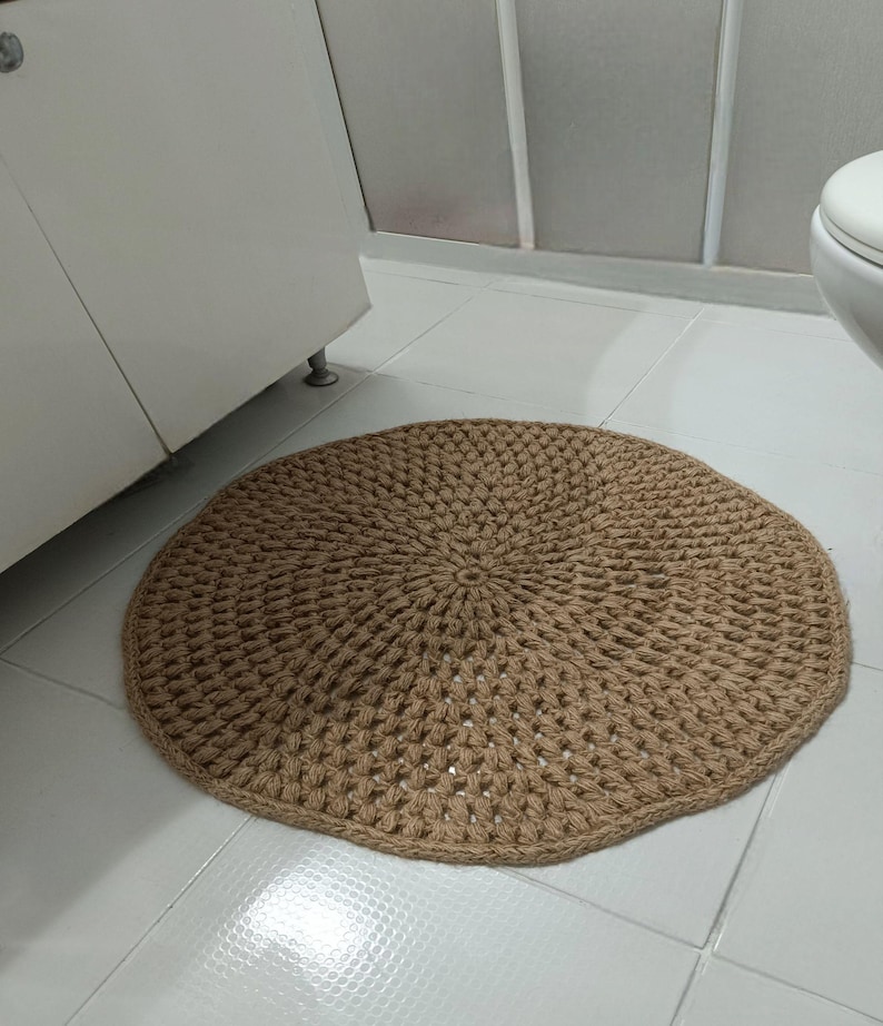 May include: A round, beige, crocheted rug with a textured pattern. The rug is made of natural fibers and has a rustic, handmade look.