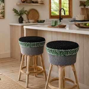 May include: Two bar stools with light-coloured wooden legs and circular seats. Each seat features a thick, textured crochet cover with a solid black top, a variegated green and white middle band, and a solid dark grey base section.