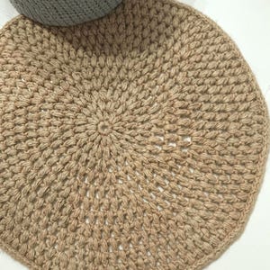 May include: A round, natural fiber rug with a crocheted design. The rug is beige and has a circular pattern.