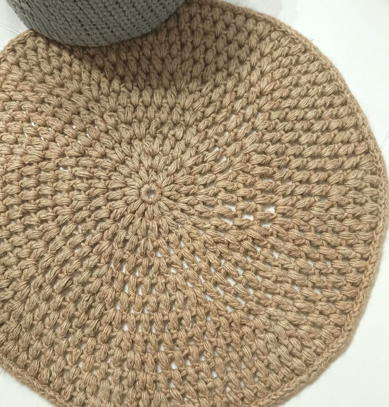 May include: A round, natural fiber rug with a crocheted design. The rug is beige and has a circular pattern.
