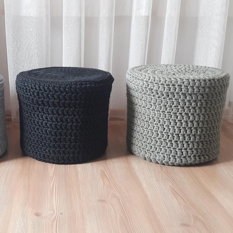 Puede incluir: Tres otomanas redondas de crochet en negro, gris y blanco. Las otomanas est&aacute;n hechas de cuerda gruesa y tienen una superficie texturizada.
