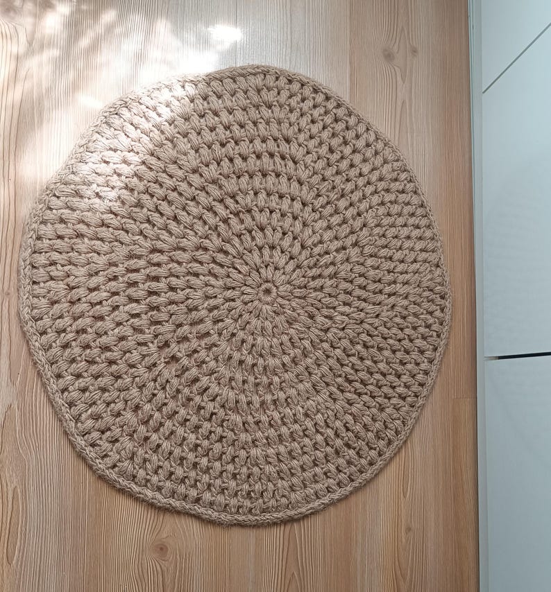 May include: A round, beige crocheted rug with a circular pattern. The rug is made of natural fibers and has a rustic, handmade look.