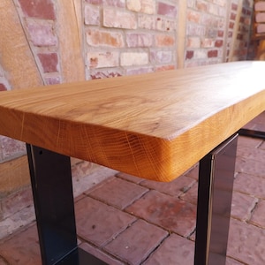 K&ouml;nnte beinhalten: Eine Holzbank mit naturbelassenem Holzfinish und schwarzen Metallbeinen. Die Bank ist aus massivem Holz gefertigt und hat einen rustikalen Look.