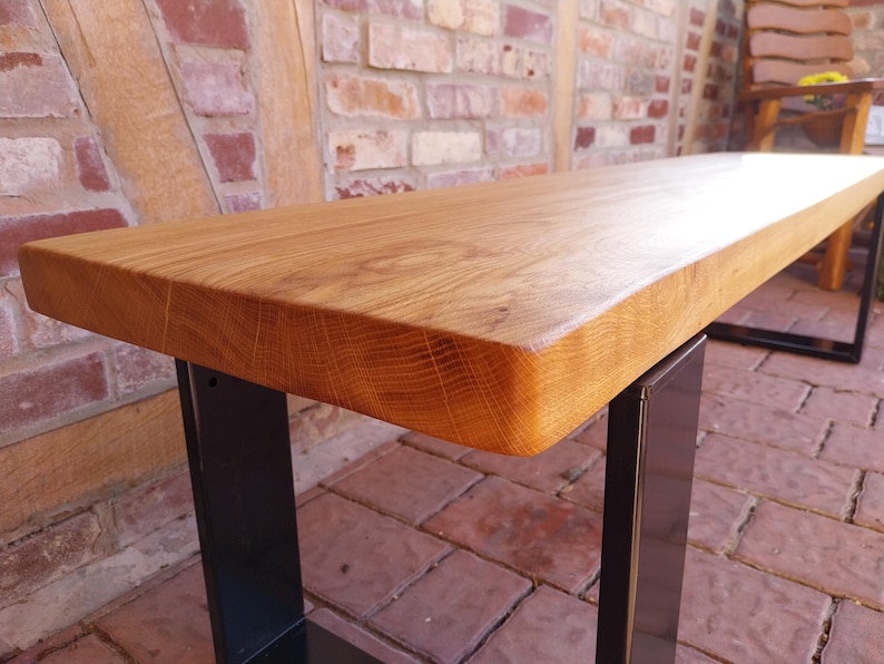 K&ouml;nnte beinhalten: Eine Holzbank mit naturbelassenem Holzfinish und schwarzen Metallbeinen. Die Bank ist aus massivem Holz gefertigt und hat einen rustikalen Look.