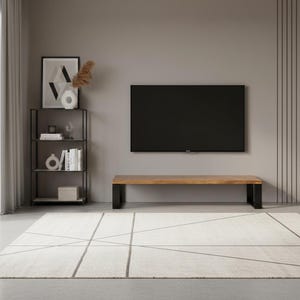 Op de afbeelding: Een moderne woonkameropstelling met een grote flatscreen-tv aan een grijze muur. Onder de tv staat een houten bank met zwarte poten. Een zwart metalen rek bevat decoratieve items. Een geometrisch patroon tapijt bedekt de vloer.