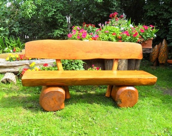 Könnte beinhalten: Eine Holzbank aus Baumstämmen mit natürlicher Oberfläche. Die Bank steht auf einem Rasen mit Blumen im Hintergrund.
