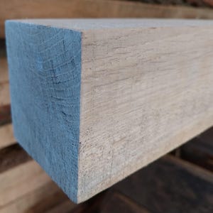 Puede incluir: Primer plano de una viga de madera de color claro con una ligera mancha azul grisácea en el extremo. La veta de la madera es visible y la viga parece ser de corte tosco.
