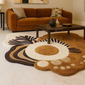 May include: A living room scene featuring a rust-colored sofa, a dark wood coffee table, and a large, floral-shaped rug in shades of brown, cream, and white. A painting with abstract shapes hangs on the wall above the sofa.