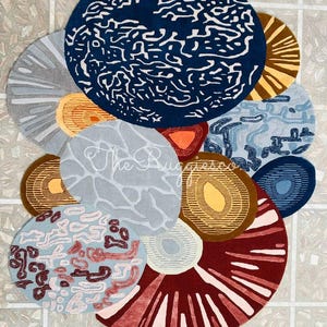 May include: A collection of circular rugs in various sizes and colors. The rugs feature abstract designs in shades of blue, gray, brown, red, and orange. Some rugs have textured patterns, while others have solid colors. The text "The Rugs Co" is visible on one rug.