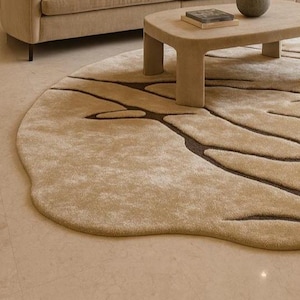 Pode incluir: Um tapete redondo bege com um design org&acirc;nico &uacute;nico. Padr&otilde;es castanhos escuros, semelhantes a veias, s&atilde;o tecidos no tapete macio de cor clara. O tapete est&aacute; colocado sobre um ch&atilde;o de azulejos claros, com um sof&aacute; e uma mesa de centro bege no fundo.
