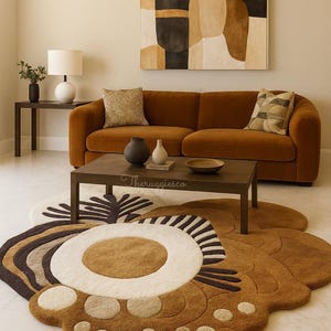 May include: A living room scene featuring a rust-colored sofa, a dark wood coffee table, and a unique rug with a floral design. The rug has a white center with brown and beige accents. An abstract painting hangs above the sofa.