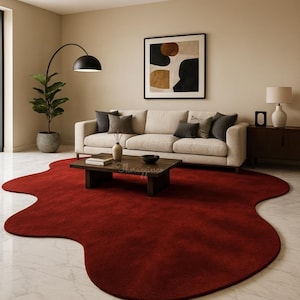 May include: A living room with a large, irregularly shaped, deep red rug. A cream sofa with grey cushions is against a neutral wall, with a dark wood coffee table in front. A black arched floor lamp and abstract art complete the scene.
