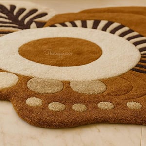 May include: Close-up of a brown, beige, and white rug with a paw print design. The rug features a circular center with a white border and a brown center. The paw has beige circles and a brown background. The rug is made of a soft, textured material.