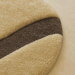 Pode incluir: Um tapete redondo e texturizado com um design de listras bege e marrom. O tapete tem uma apar&ecirc;ncia macia e felpuda, com uma borda curva. A paleta de cores &eacute; neutra, com foco em tons quentes e terrosos. Para decora&ccedil;&atilde;o de casa.