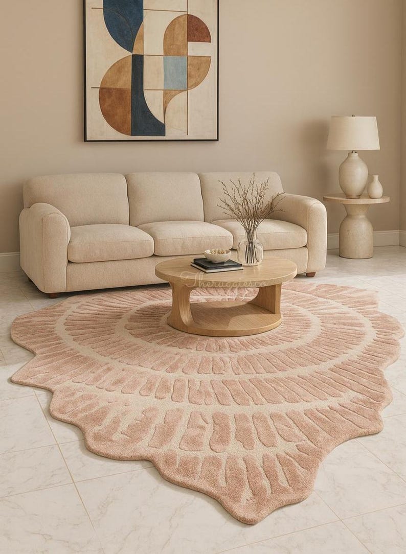 Pu&ograve; includere: Soggiorno con divano beige, tavolino in legno e tappeto rosa circolare. Il tappeto presenta un motivo dettagliato. Un dipinto con forme astratte &egrave; appeso sopra il divano. Arredamento in tonalit&agrave; neutre.