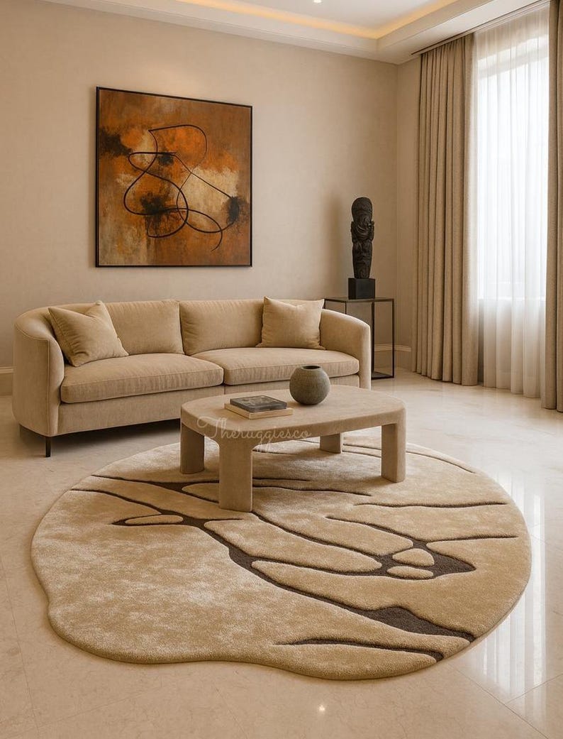 Pode incluir: Uma sala de estar com um sof&aacute; bege, uma mesa de centro redonda e um tapete estampado. Uma pintura abstrata est&aacute; pendurada acima do sof&aacute;. O tapete apresenta um design org&acirc;nico em tons de bege e castanho.