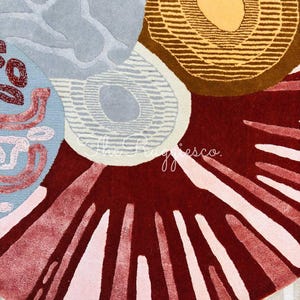 May include: A close-up of a colorful rug with an abstract design. The rug features a combination of shapes and colors, including circles, lines, and patterns in shades of red, brown, blue, and pink. The rug has a soft, textured appearance.