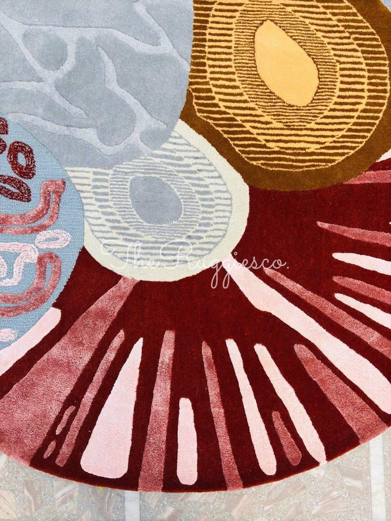 May include: A close-up of a colorful rug with an abstract design. The rug features a combination of shapes and colors, including circles, lines, and patterns in shades of red, brown, blue, and pink. The rug has a soft, textured appearance.