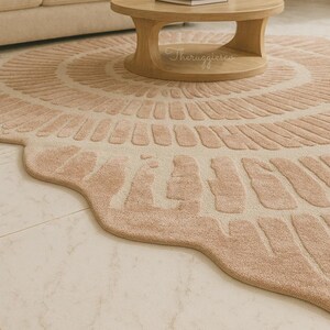 Pu&ograve; includere: Un tappeto rotondo color rosa cipria con un design unico e strutturato e bordi smerlati. Il tappeto presenta un motivo circolare centrale ed &egrave; collocato in un soggiorno con un tavolino di legno e il testo "Theruggiesco".