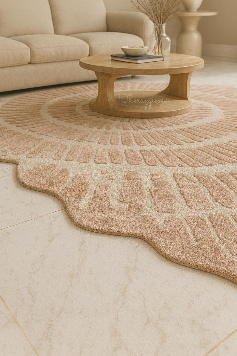 Pu&ograve; includere: Un tappeto rotondo color rosa cipria con un design unico e strutturato e bordi smerlati. Il tappeto presenta un motivo circolare centrale ed &egrave; collocato in un soggiorno con un tavolino di legno e il testo "Theruggiesco".